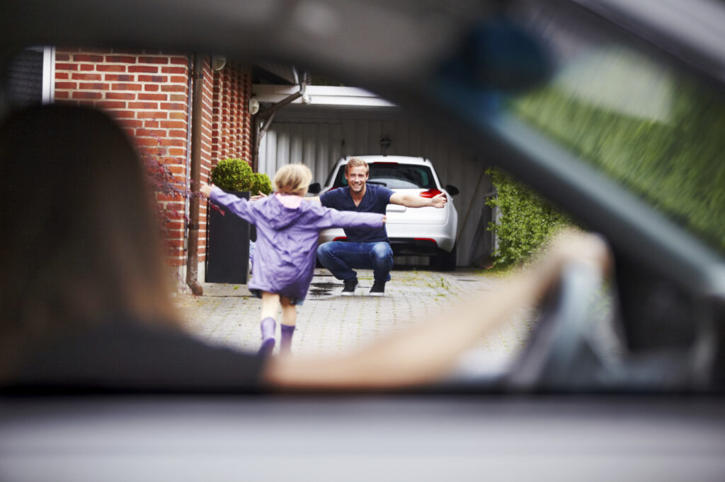 Cute little girl running towards her dad as her mom looks on from the car