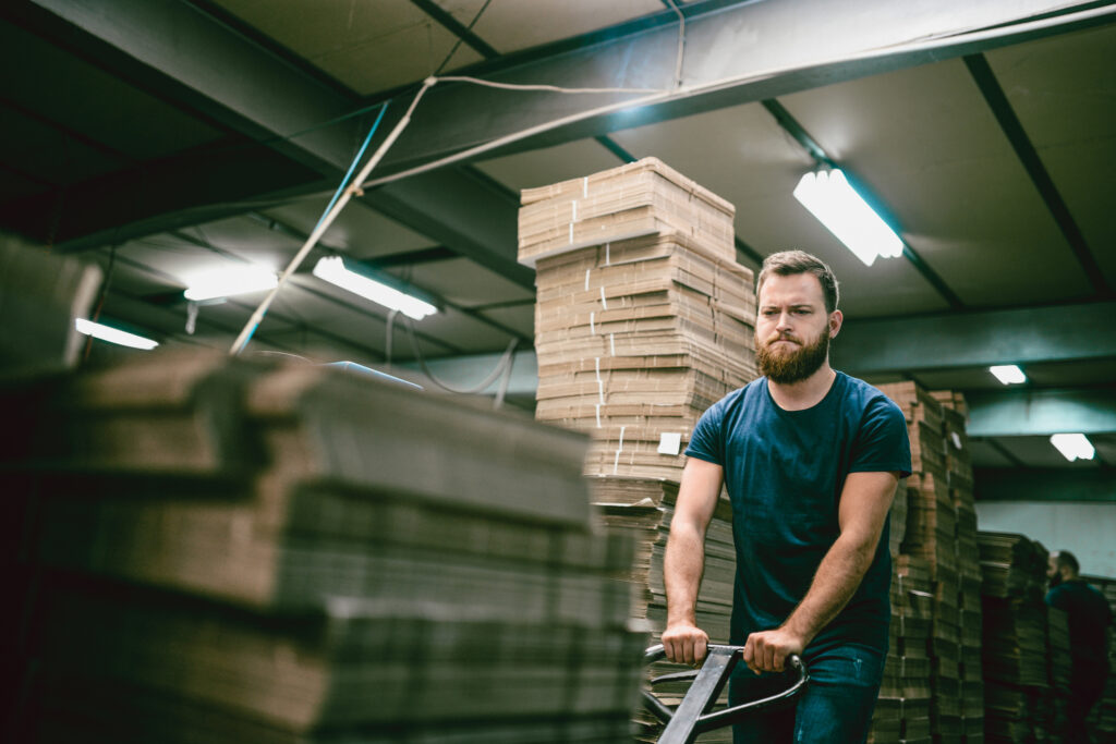 Nervous Worker Pushing Cardboard Carton Planks On Transportation Cart on Night Shift