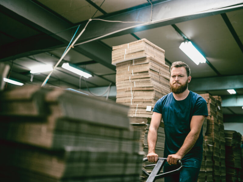 Nervous Worker Pushing Cardboard Carton Planks On Transportation Cart on Night Shift